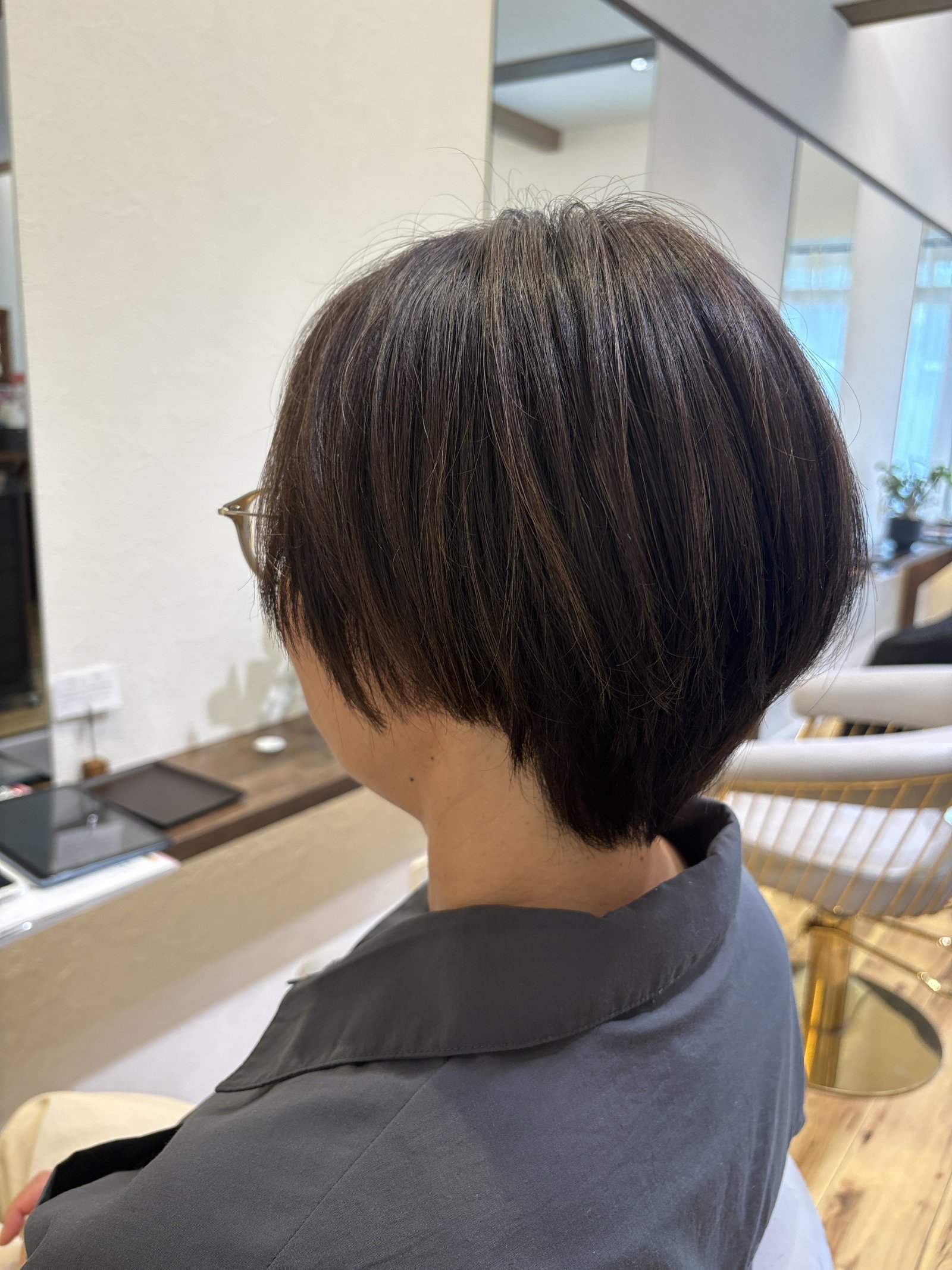 ハイライトが溶け込むダークブラウンの丸みショートボブ=耳かけで軽やかな横顔を斜め横から