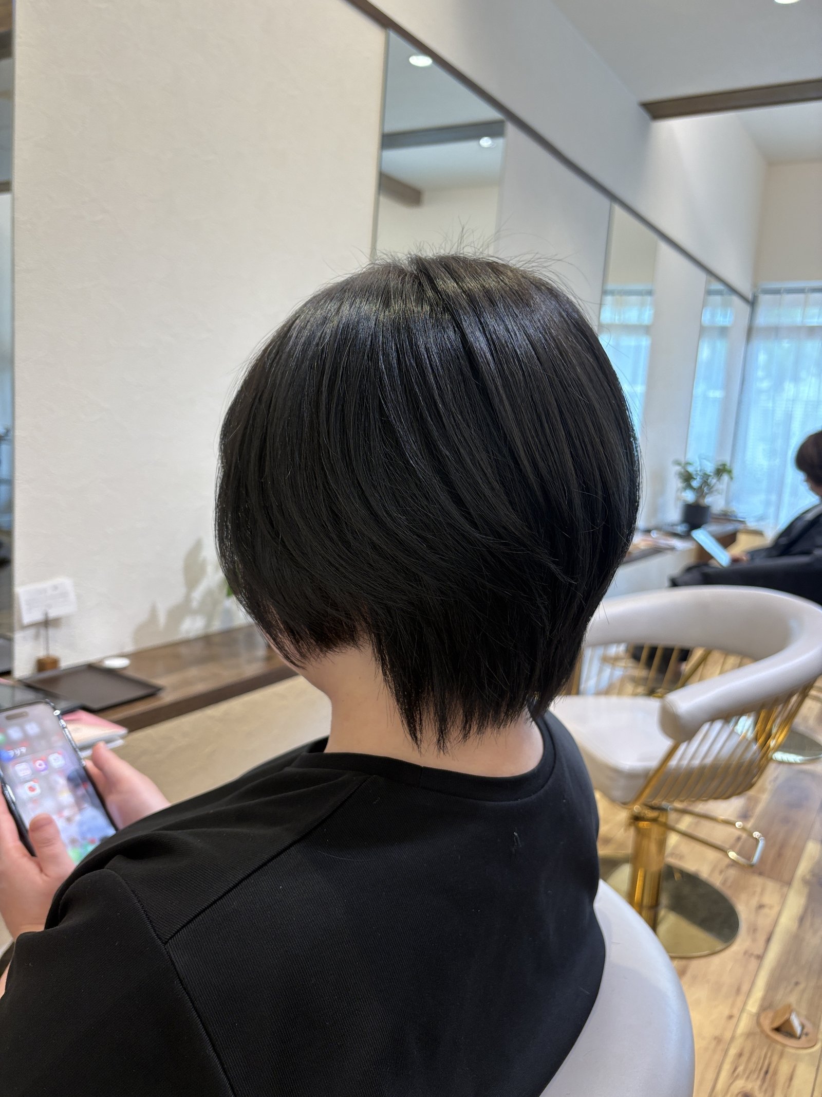 黒髪のハンサムショート=襟足をタイトに収めた首すじと、後頭部の丸みのシルエットを斜め後ろから