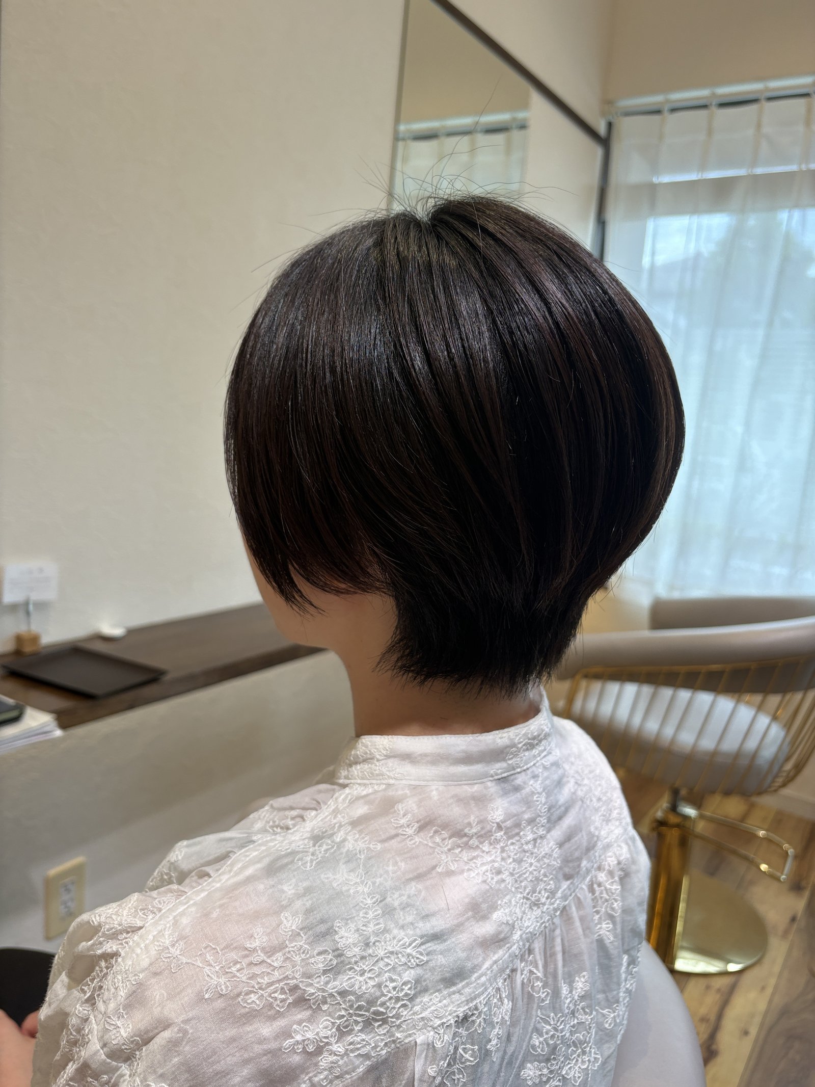 ダークブラウンの丸みショートボブ=耳の下あたりの長さで後頭部にふんわり丸みをつくり、襟足をコンパクトに収めた大人のショートボブを斜め横から