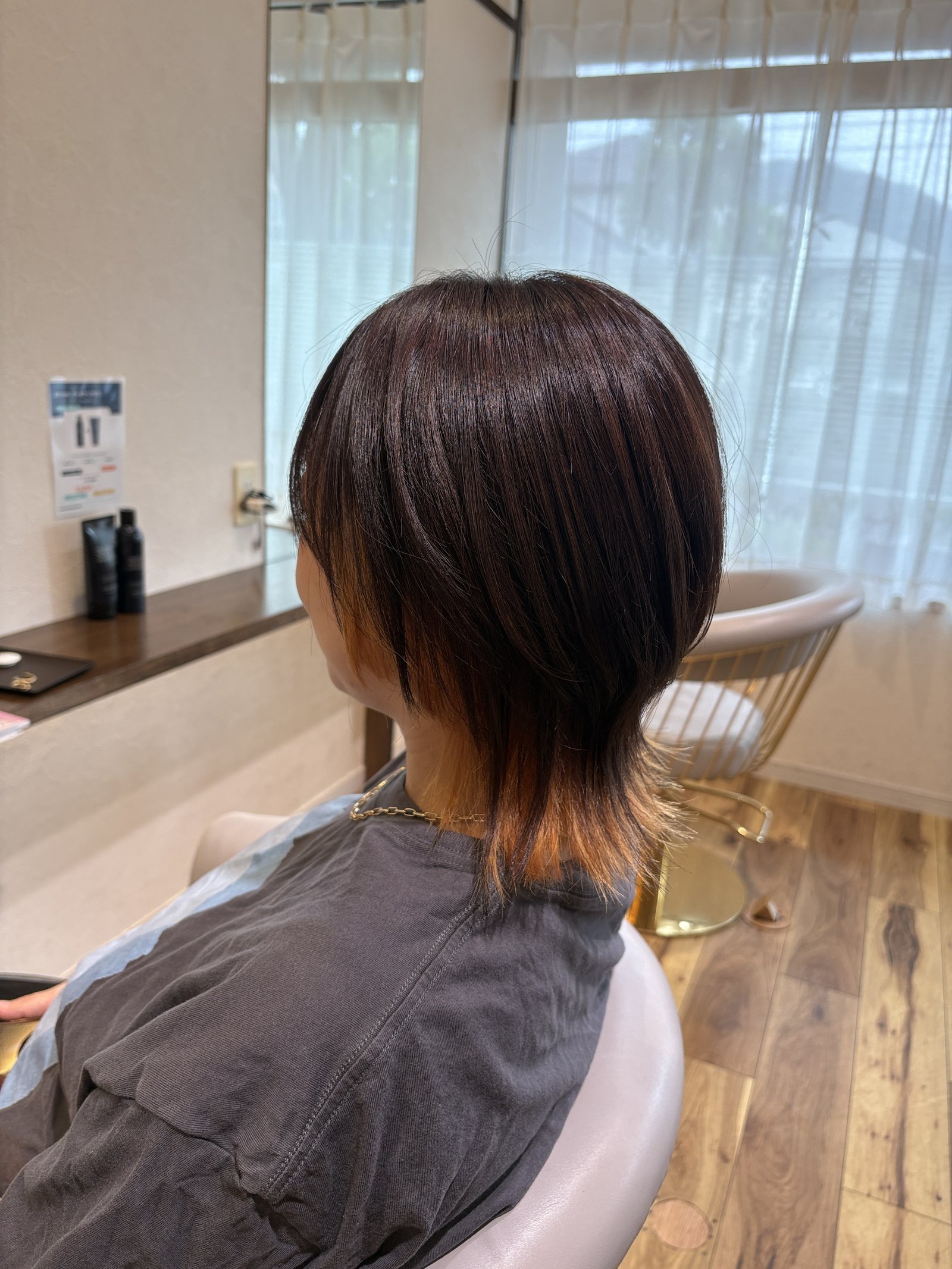 ダークブラウンのショートウルフ=表面はレイヤーで丸みと動きをつくり、襟足の内側にブリーチインナーを仕込んだ大人のウルフを斜め横から