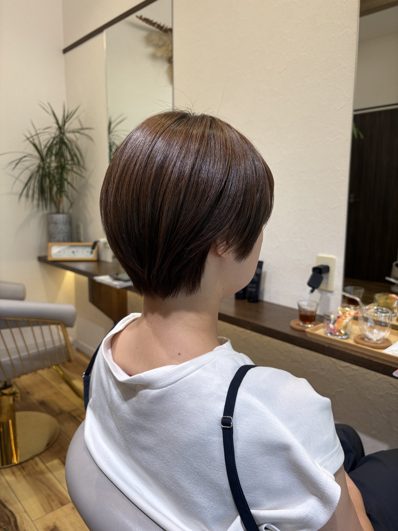 明るめベージュの大人の丸みショート|表面のツヤと、首に沿ってタイトに締めたえり足、右からの斜め後ろ