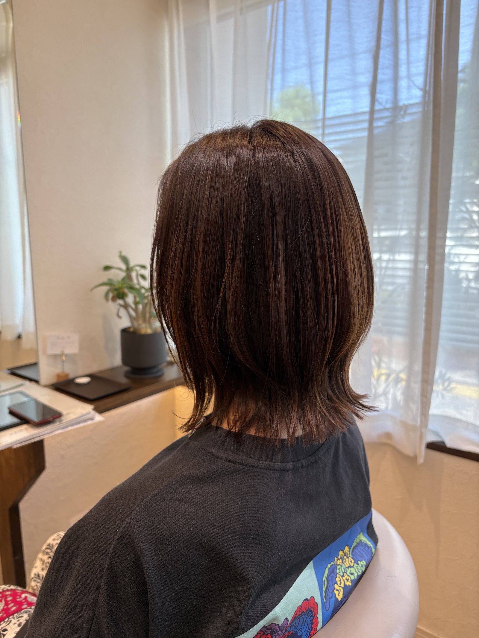 ピンクブラウンベージュのくびれミディアム|毛先の段と首もとのくびれ、毛先に向けて軽く透ける色を窓側の斜め後ろから
